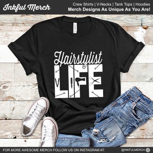 Può includere: Maglietta nera con testo bianco che recita "Hairstylist Life" e presenta strumenti da parrucchiere come forbici, fermagli per capelli e un asciugacapelli.