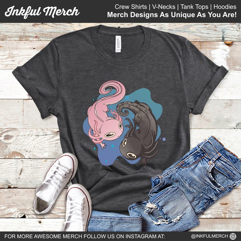 K&ouml;nnte beinhalten: Dunkelgraues T-Shirt mit einem rosa und schwarzen Axolotl-Design. Die Axolotl sind vor einem blau-t&uuml;rkisfarbenen Hintergrund platziert. Das Shirt tr&auml;gt auch den Text "Inkful Merch" und "Merch Designs As Unique As You Are!"
