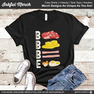 May include: Black t-shirt with a white graphic of the word "BOBBE" with illustrations of beef, butter, bacon, and eggs. The text stands for "Beef, Butter, Bacon, Eggs".