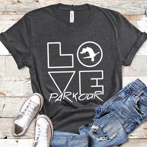 May include: A dark gray t-shirt with a white graphic design that says "LOVE PARKOUR" with a silhouette of a person doing a parkour move inside a circle.
