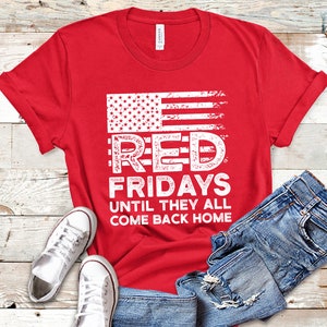 May include: Red t-shirt with a distressed American flag graphic and the text "Red Fridays Until They All Come Back Home".