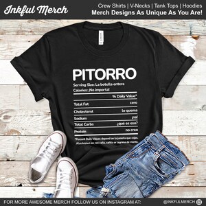 Può includere: Maglietta nera con una grafica bianca di un'etichetta di informazioni nutrizionali. L'etichetta è intitolata "Pitorro" e include il testo "Serving Size: La botella entera" e "Calories: ¡No importa!"  L'etichetta elenca le seguenti informazioni nutrizionali: Grassi totali, Colesterolo, Sodio, Carboidrati totali e Proteine. Ogni elemento ha una frase in spagnolo accanto.