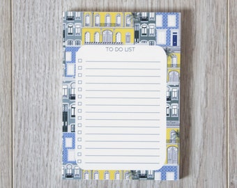 May include: A white notepad with a blue and yellow patterned cover featuring a cityscape. The notepad has a to-do list heading and a lined section with checkboxes.