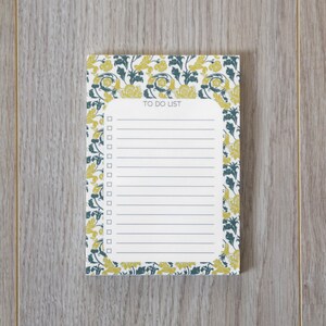 May include: A white notepad with a floral border in shades of yellow and green. The notepad has a lined section with the words "TO DO LIST" at the top.