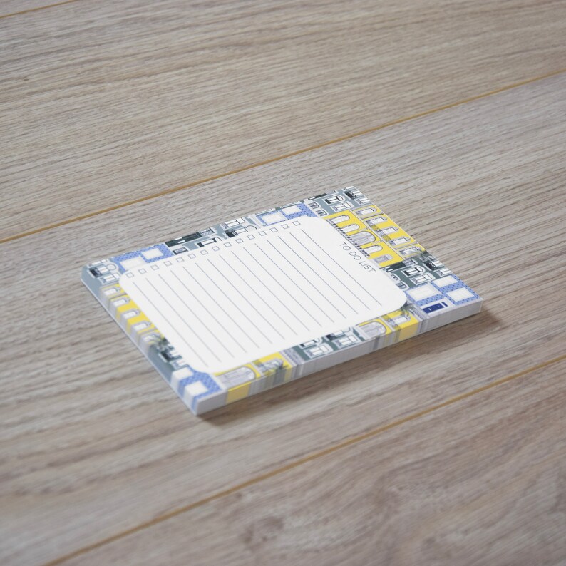May include: A small notepad with a white lined page and a colourful patterned cover. The cover features a repeating pattern of blue and yellow buildings with the words "To Do List" printed in yellow.