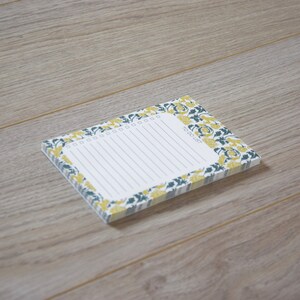 May include: A white notepad with a floral border in shades of yellow and green. The notepad has a lined interior and the text "To Do List" printed on the front.