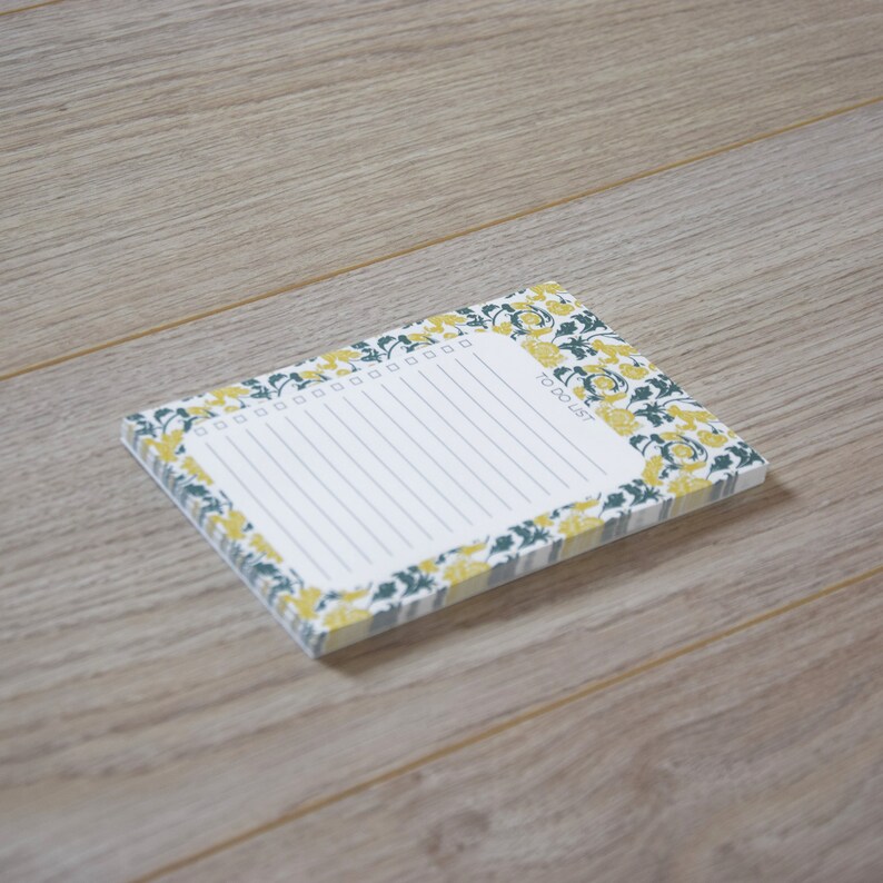 May include: A white notepad with a floral border in shades of yellow and green. The notepad has a lined interior and the text "To Do List" printed on the front.