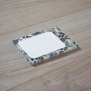 May include: A white notepad with a green and white floral design. The notepad has a to-do list heading and a lined section for writing.