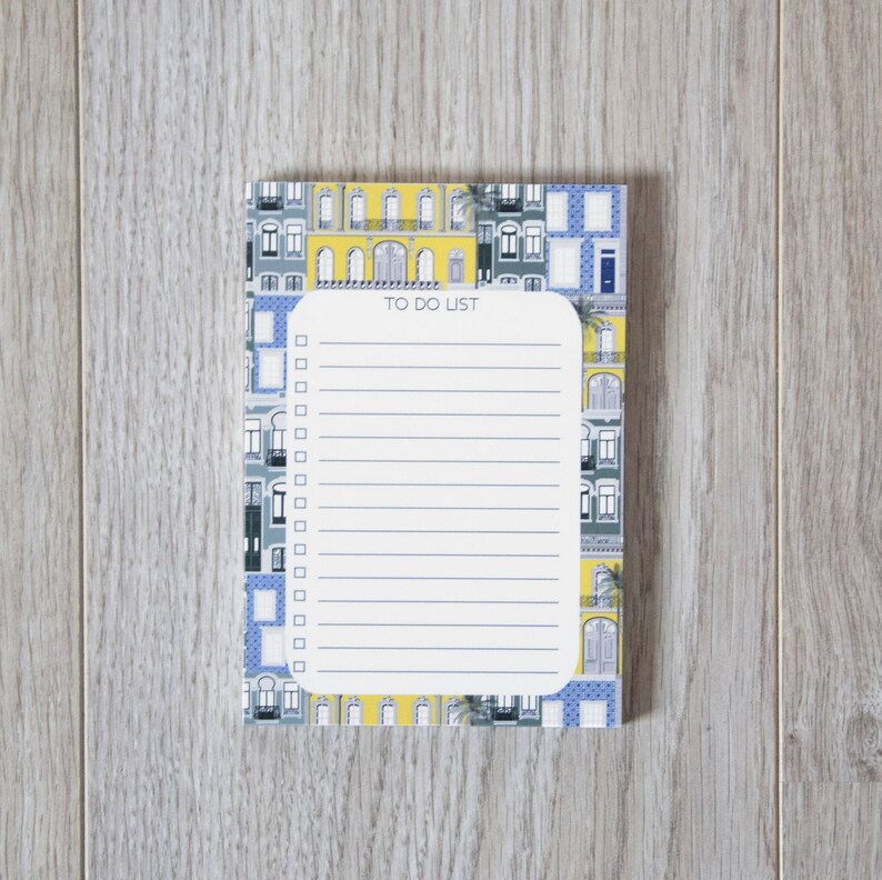 May include: A white notepad with a blue and yellow patterned cover featuring a cityscape. The notepad has a to-do list heading and a lined section with checkboxes.