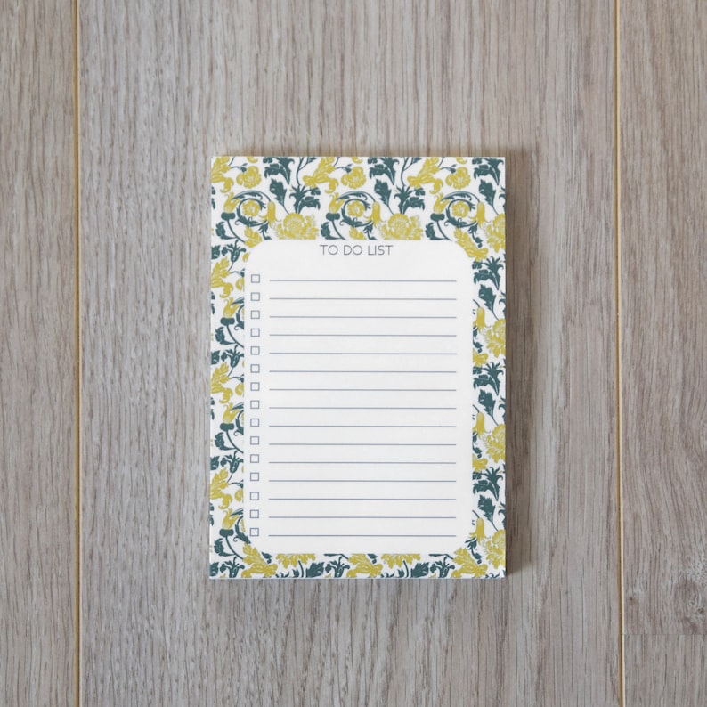 May include: A white notepad with a floral border in shades of yellow and green. The notepad has a lined section with the words "TO DO LIST" at the top.