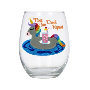 May include: A clear glass wine glass with a colorful unicorn design. The unicorn is floating on a pool float with a drink in its hand. The text "Float Tan Drink Repeat" is printed on the glass.