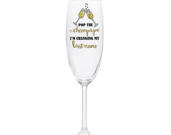 Puede incluir: Una flauta de champán transparente con una inscripción dorada que dice "Pop the champagne I'm changing my last name".