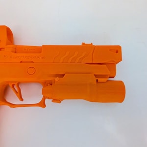 May include: Bright orange handgun with a mounted light and sight. The firearm has a textured grip and a trigger guard. The slide features a series of angled grooves. The text "X-Werks Tactical Arms" is visible on the slide.