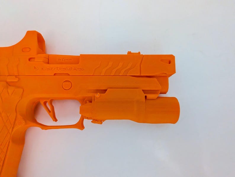 May include: Bright orange handgun with a mounted light and sight. The firearm has a textured grip and a trigger guard. The slide features a series of angled grooves. The text "X-Werks Tactical Arms" is visible on the slide.