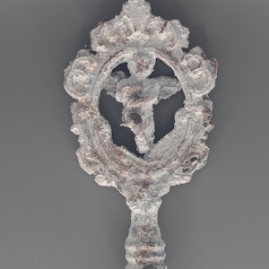 May include: A decorative, ornate key with a white, textured finish and a detailed design. The key features a circular emblem with a central figure and intricate scrollwork, set against a gray background.