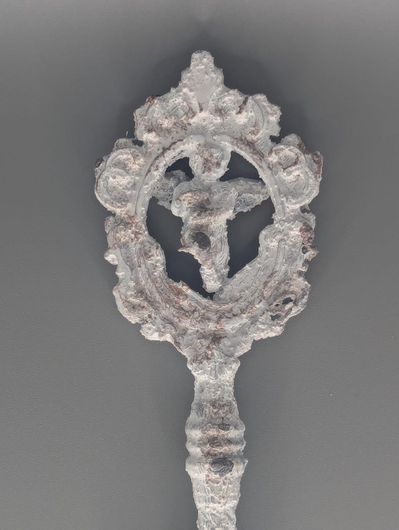 May include: A decorative, ornate key with a white, textured finish and a detailed design. The key features a circular emblem with a central figure and intricate scrollwork, set against a gray background.
