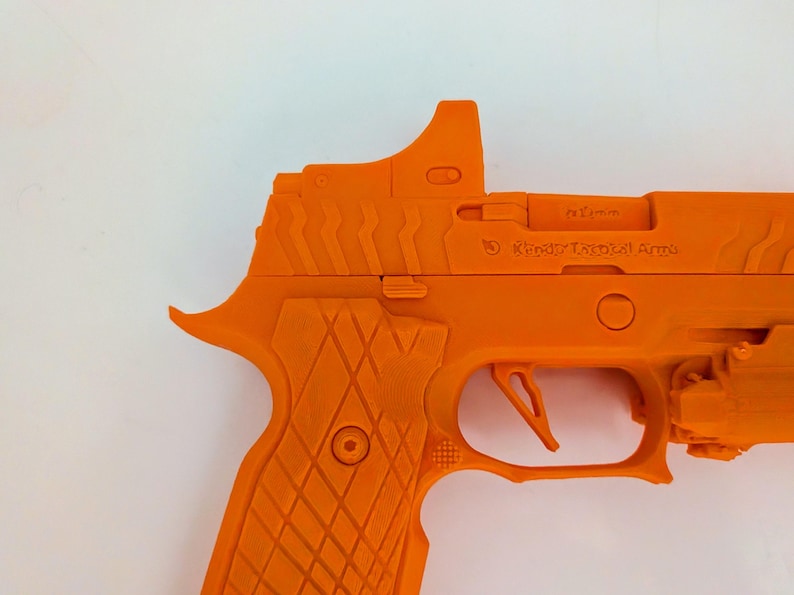 May include: Bright orange handgun with a textured grip and a sight on top. The gun features a trigger, a slide, and the text "Kandy Tactical Arms". The overall design is angular and modern.
