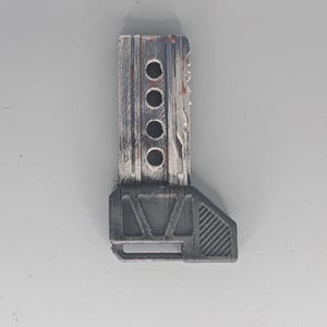 May include: A weathered, rectangular object with a dark gray base and a wooden-like top. The top section has four circular holes and a distressed, painted finish with hints of red. The base has a geometric design.