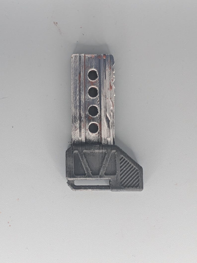 May include: A weathered, rectangular object with a dark gray base and a wooden-like top. The top section has four circular holes and a distressed, painted finish with hints of red. The base has a geometric design.