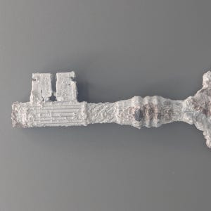 May include: A decorative, oversized key with a textured, aged appearance. The key is primarily white with hints of brown and gray, suggesting a weathered or antique finish. The key's design is ornate, with a detailed handle and a classic key shape.