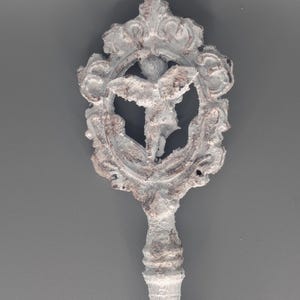 May include: A decorative key with a detailed, ornate design. The key features a white and brown color scheme with a central emblem of a figure within a circular frame. The handle has a textured, twisted pattern.