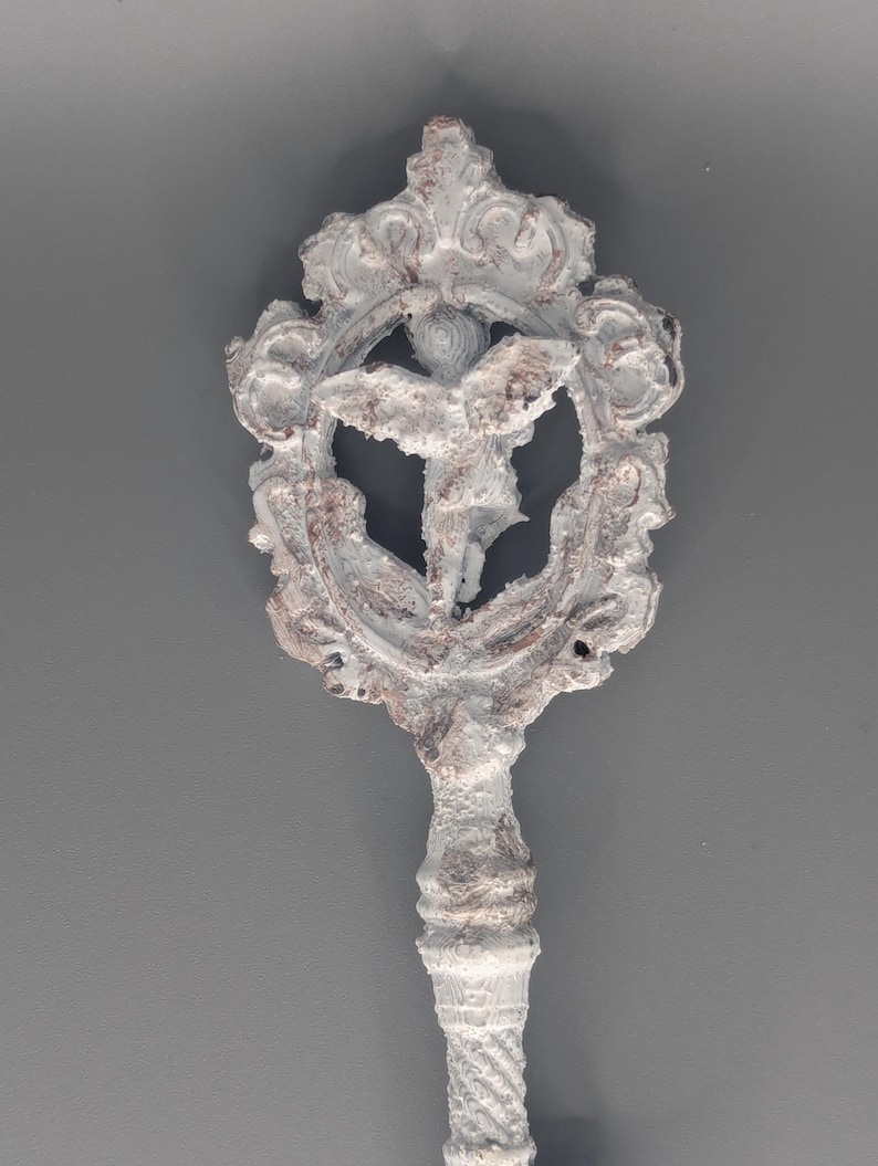 May include: A decorative key with a detailed, ornate design. The key features a white and brown color scheme with a central emblem of a figure within a circular frame. The handle has a textured, twisted pattern.