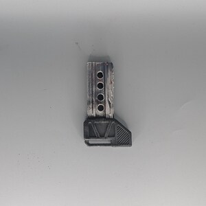 May include: A small, gray and black tool with a rectangular wooden top section featuring four circular holes. The bottom section is a dark gray, angled shape. The tool appears to be made of wood and plastic.