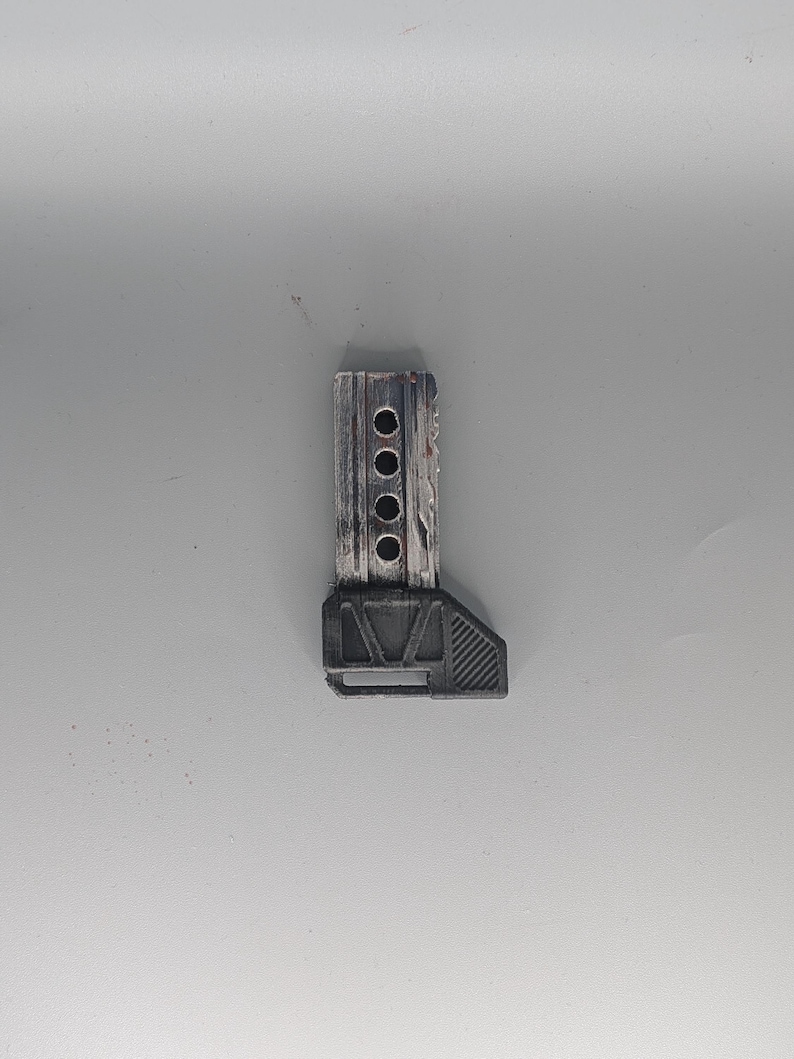 May include: A small, gray and black tool with a rectangular wooden top section featuring four circular holes. The bottom section is a dark gray, angled shape. The tool appears to be made of wood and plastic.