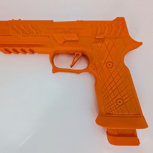 May include: Bright orange handgun with the text "ALLIGATOR SNAPPER" on the side. The grip has a diamond pattern, and the gun has a magazine. The trigger and other details are clearly visible.