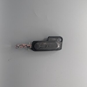 May include: A black key with a silver, patterned blade. The key has a rectangular head with a circular hole and a small, circular indentation. The key is likely for a door or lock.