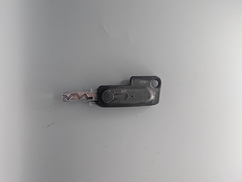 May include: A black key with a silver, patterned blade. The key has a rectangular head with a circular hole and a small, circular indentation. The key is likely for a door or lock.