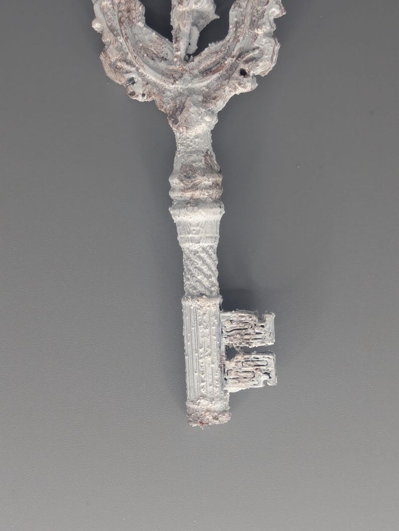 May include: An ornate, antique-style key with a detailed, decorative head and a textured, ridged handle. The key is primarily white with brown accents, suggesting an aged or weathered appearance. The key's design evokes a vintage aesthetic.