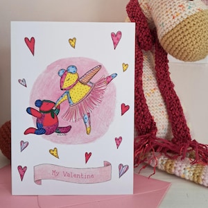 May include: A Valentine's Day card featuring a watercolour illustration of two dancing teddy bears. One bear is dressed as a ballerina in a pink tutu. The card has the text "My Valentine" on a banner, surrounded by hearts.