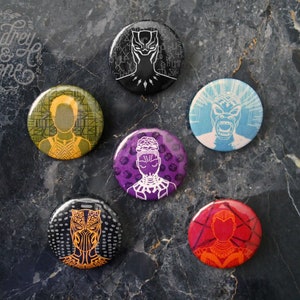 Pode incluir: Conjunto de seis botões redondos preto e branco com personagens do filme Pantera Negra. Os botões são impressos com imagens de Pantera Negra, Okoye, Nakia, Shuri, M'Baku e Erik Killmonger.