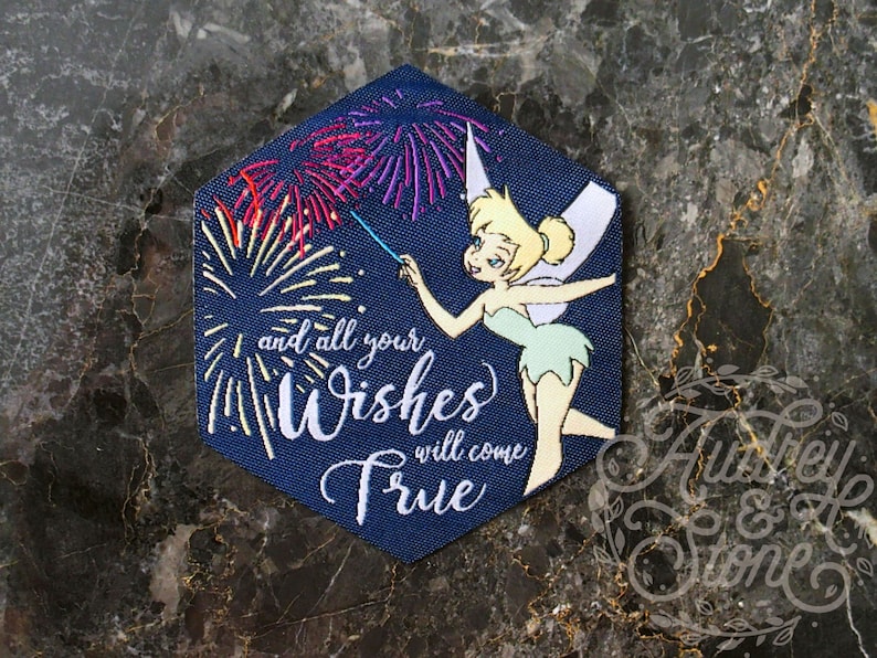 Pu&ograve; includere: Una toppa esagonale blu con un personaggio di Trilly che tiene una bacchetta magica con fuochi d'artificio. Il testo sulla toppa recita "and all your Wishes will come True".