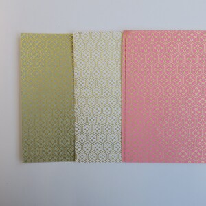 Puede incluir: Tres hojas de papel decorativo con un patr&oacute;n geom&eacute;trico en oro sobre un fondo verde, blanco y rosa.