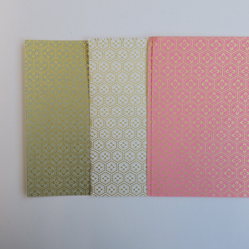 Puede incluir: Tres hojas de papel decorativo con un patr&oacute;n geom&eacute;trico en oro sobre un fondo verde, blanco y rosa.
