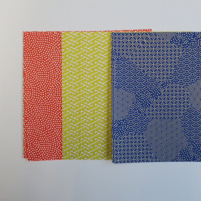 Puede incluir: Tres hojas de papel japon&eacute;s decorativo con diferentes patrones. La primera hoja es roja con lunares blancos, la segunda hoja es amarilla con un patr&oacute;n geom&eacute;trico blanco y la tercera hoja es azul con un patr&oacute;n geom&eacute;trico dorado.