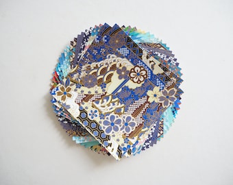 May include: A stack of colorful patterned origami paper squares, featuring blue, gold, and white designs. The paper is arranged in a circular pattern, with the top square showing a floral and wave design.