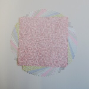 Puede incluir: Una pila de cuadrados de papel de colores con patrones, con un cuadrado rosa con puntos blancos en la parte superior. Los cuadrados est&aacute;n dispuestos en forma de abanico.