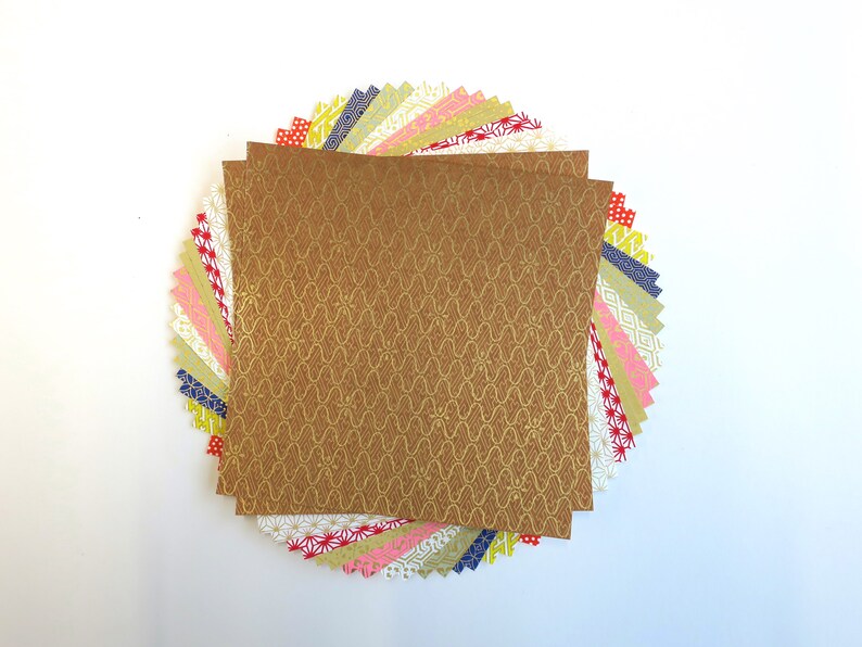 Puede incluir: Una pila de papel de origami con patrones coloridos con una sola hoja de papel dorado con un patr&oacute;n repetitivo en la parte superior.