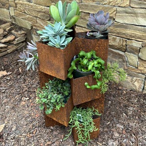 May include: A rusty metal planter with six compartments, each holding a different type of succulent plant. The planter is made of recycled metal and has a rustic, industrial look.