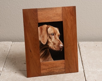 May include: A rectangular wooden picture frame with a portrait of a brown dog. The frame is made of dark wood and has a simple, classic design. The dog is in profile, with a black background.