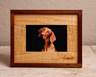 May include: A wooden picture frame with a reddish-brown outer frame and a lighter wood inner frame. A photo of a brown dog with its head tilted to the side is inside the frame.