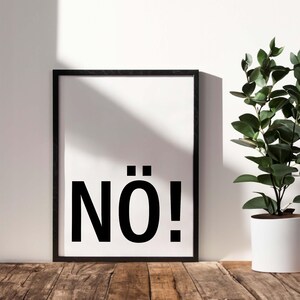 May include: A black framed poster with the word "N&Ouml;!" printed in bold, black letters on a white background. The poster is hanging on a white wall with a potted plant in the background.