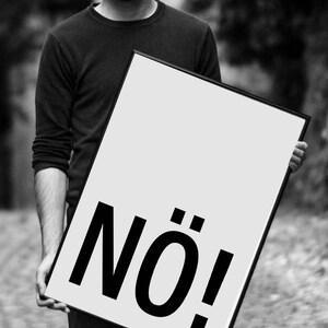 May include: A black and white image of a person holding a poster with the word "N&Ouml;!" printed in bold, black letters.