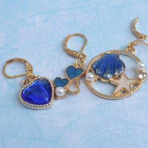 Peut inclure: Une paire de boucles d'oreilles en or avec des accents en émail bleu et blanc. Une boucle d'oreille présente un coquillage bleu et une étoile de mer blanche, tandis que l'autre boucle d'oreille a un bijou bleu en forme de cœur.