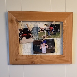 May include: A wooden picture frame with a wire mesh backing holds a collection of personal photos. The photos show a young boy playing in a pool, a man and a young girl standing in front of a truck, and a young girl wearing a blue hat.