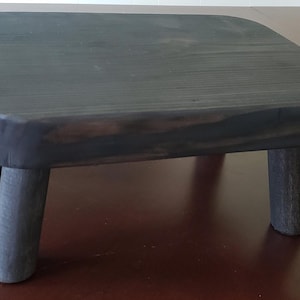 May include: A dark gray wooden stool with four legs. The stool is made of solid wood and has a smooth, polished finish.