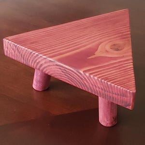 May include: A triangular wooden stand with three legs. The stand is painted a deep red color and has a natural wood grain pattern.